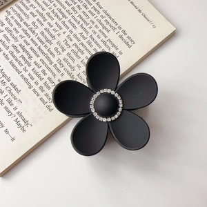 Detail of matte black floral hair claw clip with rhinestones on an open book
