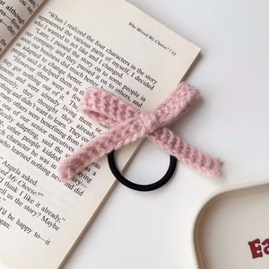 Nahaufnahme eines rosa gestrickten Haargummis mit Zopfmuster auf einem offenen Buch