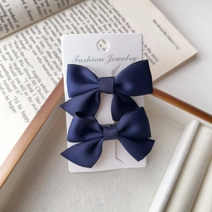 Detail of two dark blue satin bow hair clips displayed on a professional white card