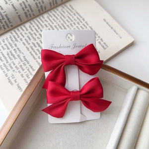 Close-up of two red satin bow hair clips on a jewelry display card in a wooden tray