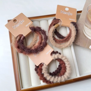 Set di tre elastici per capelli in peluche nei toni caldi su vassoio in legno