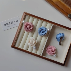 Détail de pinces à cheveux camélia en tissu avec perles dans une boîte à bijoux en bois