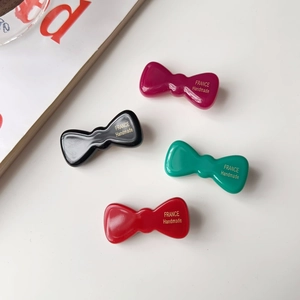 Détail de quatre barrettes nœuds en acétate en noir, rouge et vert avec texte doré fait main