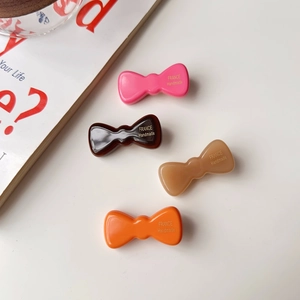 Détail de quatre barrettes nœuds en acétate fait main avec lettrage doré sur fond crème