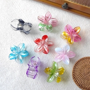 Detailed set of 8 colorful plumeria flower claw clips and resin hair slides on white fabric