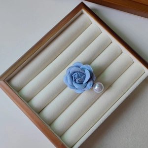 Détail d'une broche camélia en tissu bleu avec une grande perle blanche dans un coffret