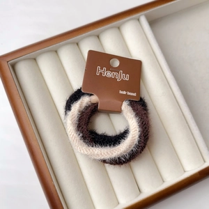 Primo piano di elastici per capelli in peluche nero, marrone e crema su vassoio in legno
