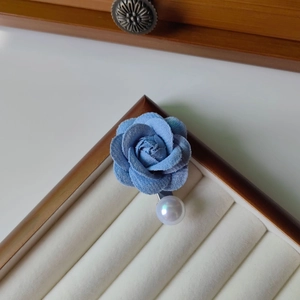 Détail d'une broche rose en velours bleu avec perle blanche sur boîte à bijoux