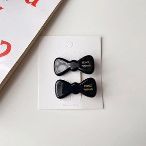 Détail de deux barrettes à nœud noir brillant sur carte avec lettrage doré fait main