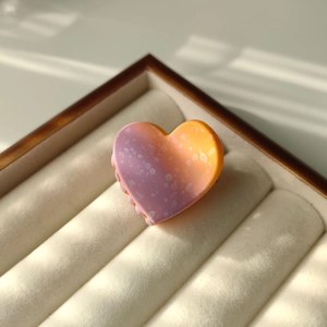 Detail of purple-orange gradient heart hair claw with white polka dots on velvet tray