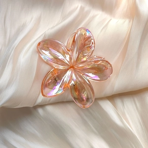 Detail of peach flower hair claw clip with iridescent finish on soft satin background