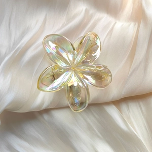 Macro detail of translucent iridescent plumeria flower hair claw clip on soft satin fabric