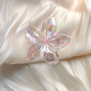 Detailed macro view of pink iridescent plumeria flower hair claw clip with golden spring