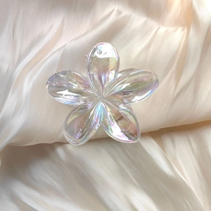 Close-up of iridescent frangipani hair claw clip on soft beige silk fabric background