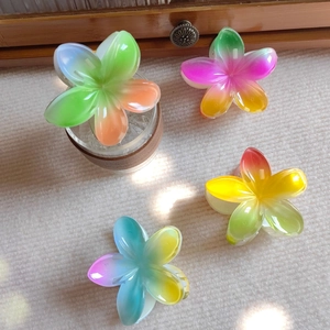 Close-up of four colorful gradient resin plumeria flower hair claws on textured fabric