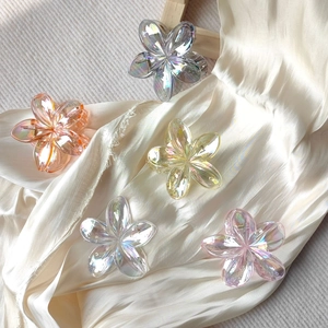 Flat lay of five transparent gradient flower hair claws on elegant silk fabric