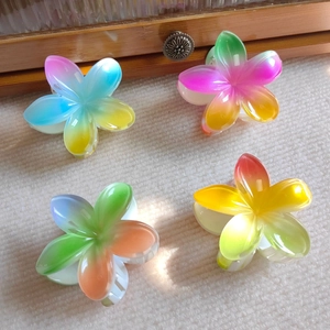 Close-up of four gradient plumeria hair claws with a translucent jelly texture on fabric