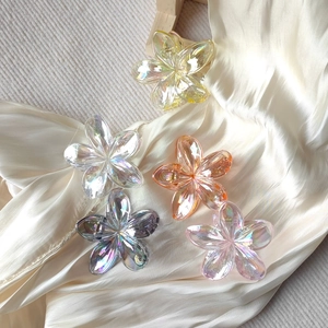 Detailed view of five iridescent resin flower hair claws on cream silk background