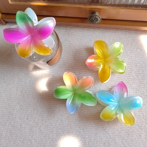 Close-up of four colorful gradient resin plumeria flower hair claws on a white surface