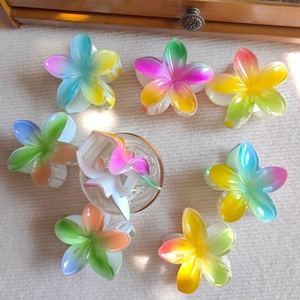Top view of vibrant gradient resin frangipani flower hair claws on beige carpet