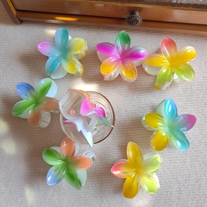 Flat lay of eight colorful gradient plumeria hair claws on a textured surface