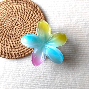 Detail of three-color gradient plumeria hair claw clip on a rustic woven mat background