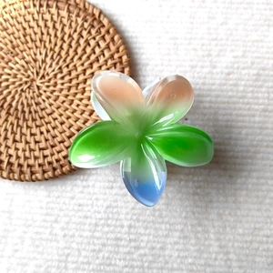 Detail view of pink and blue gradient plumeria hair claw clip on a textured background