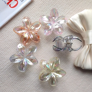 Detailed close-up of iridescent plumeria hair claws and floral clips on a textured background