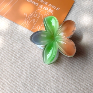 Detail view of a translucent plumeria hair claw clip with green and blue resin petals