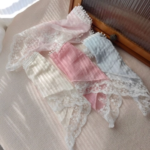Detail of four colorful lace triangle scarves with pom-poms in pink, white, and blue