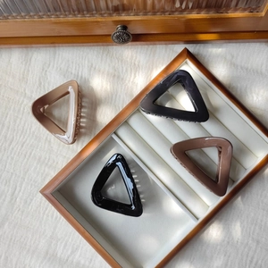 Close-up of triangle hair claw clips in black and brown on a wooden display tray