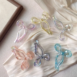 Detailed view of six colorful bow-shaped hair claws with holographic finish on silk fabric