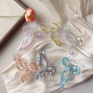Close-up of six colorful laser bow hair clips on a beige silk background