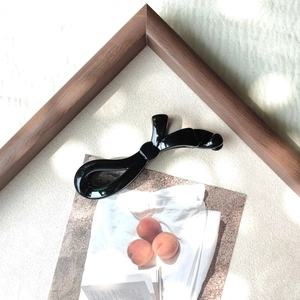 Gros plan d'une pince banane noire brillante avec un design à nœud élégant sur cadre en bois