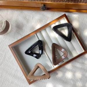 Detail view of triangular hair claw clips in four neutral earth-toned colors on a tray