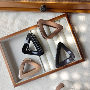 Close-up of four glossy triangular hair claws in black, brown, grey, and cream on a tray