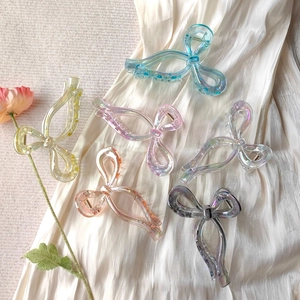 Detail of six iridescent bow hair clips in assorted pastel colors on satin fabric