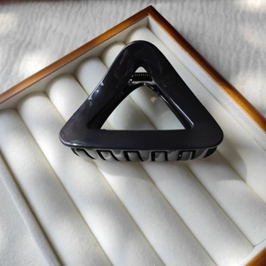 Detailed view of a sleek black triangular hair claw clip on a luxury jewelry display tray