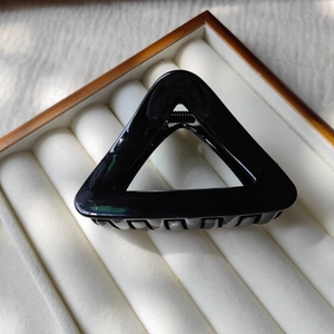 Detail view of a black glossy triangle hair claw clip with metal spring on velvet