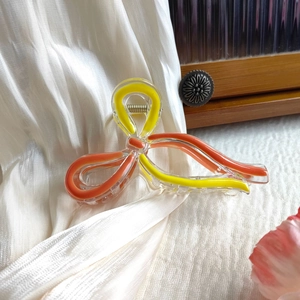 Detailed close-up of orange acrylic butterfly hair claw clip on white satin fabric