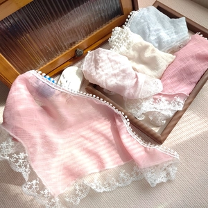 Pastel lace-trimmed triangular headscarves in pink, beige and blue on a wooden tray
