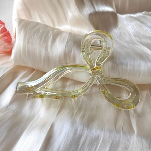 Macro shot of iridescent pale yellow acrylic bow hair claw clip on silk fabric