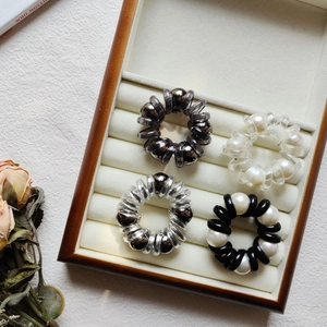 Close-up of pearl spiral hair ties in black, silver, and bronze on white velvet