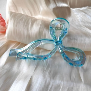 Close-up of iridescent light blue bow hair claw clip on white silk fabric background