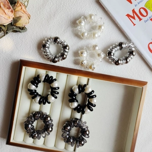Detail of pearl telephone cord hair ties in black and silver on a wooden display tray