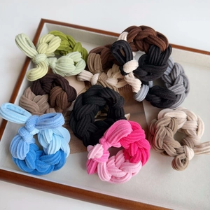 Close-up of colorful braided elastic hair ties with ribbed fabric texture in a wooden tray