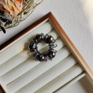 Deep gray spiral hair tie with metallic beads inside a jewelry box with dried flowers