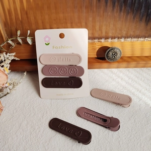 Dettaglio di fermagli opachi con goffratura Hello e Love in tonalità terra naturali