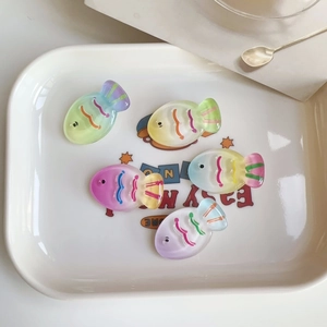 Close-up of colorful gradient resin fish hair clips in a white ceramic dish