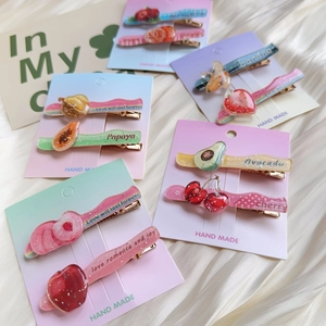 Detail of glittery acrylic fruit hair clips with gold metal base on silk background